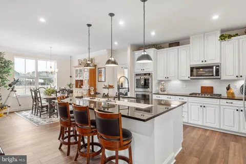 a kitchen with stainless steel appliances kitchen island granite countertop a sink a stove a refrigerator and white cabinets with wooden floor