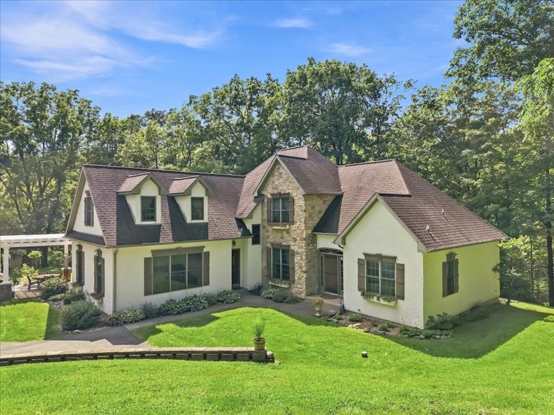 Mature trees frame a multi-level facade showcasing elegant stone accents and dormer windows.