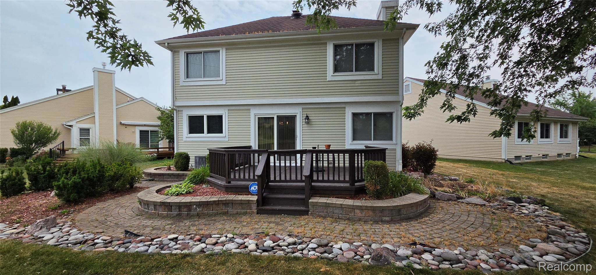 380 Huntington Court Rochester, MI 48307 - Photo 2 of 26 Two-story exterior with light-colored siding, a multi-tiered wooden deck, and a paver patio with decorative rock borders