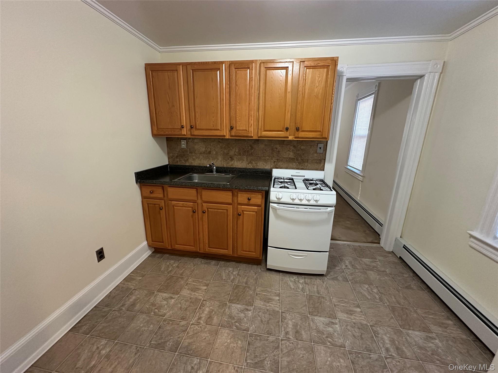 18 West Maple Avenue Suffern, NY 10901 - Photo 4 of 24 Kitchen featuring white gas stove, baseboard heating, brown cabinets, dark countertops, and ornamental molding