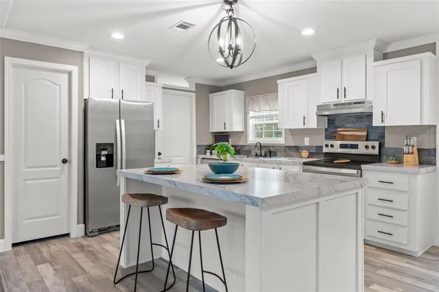 a kitchen with stainless steel appliances granite countertop a refrigerator a sink dishwasher a stove a microwave oven a dining table and chairs with wooden floor