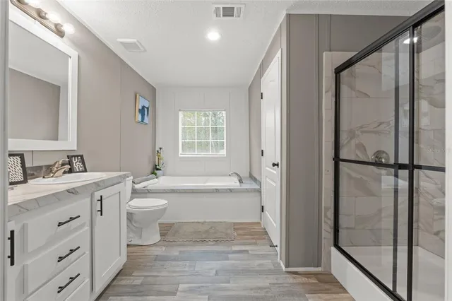 a bathroom with a granite countertop toilet a sink a mirror a bathtub and window