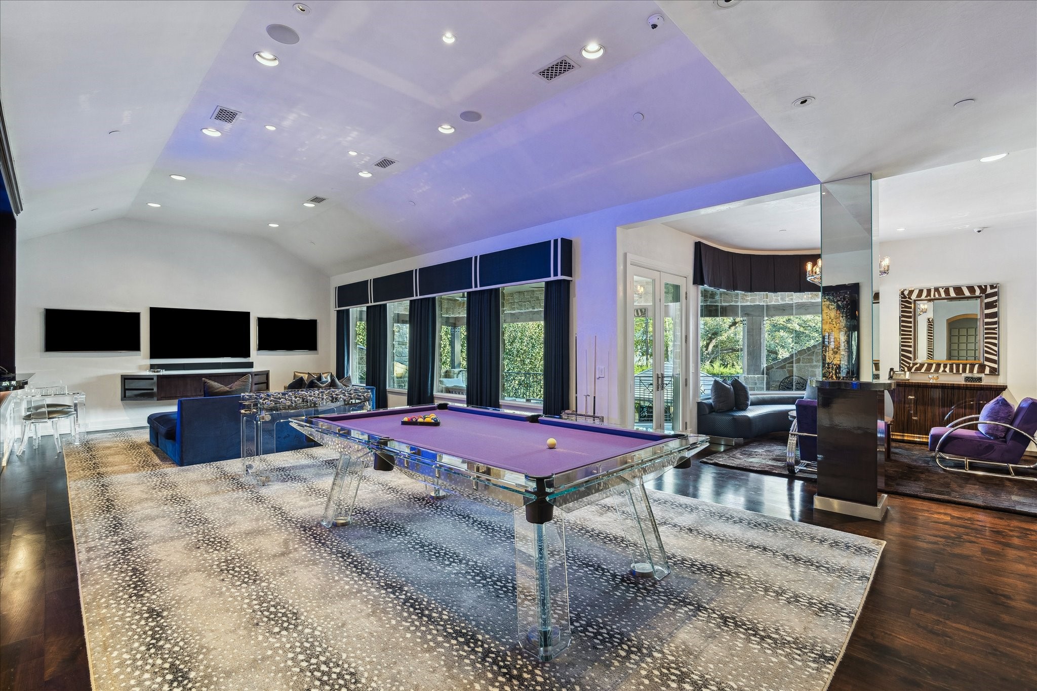 220 Merrie Way Lane Houston, TX 77024 - Photo 33 of 50 The game room features wide-plank oak flooring and Segreto-plastered walls and ceiling, anchored by a floating Macassar ebony media cabinet. Four large picture windows with remote-controlled designer coverings open to views of the private balcony, while an oak-cased opening leads seamlessly into the screening room. Recessed LED lighting and in-ceiling speakers complete this elevated entertainment space.