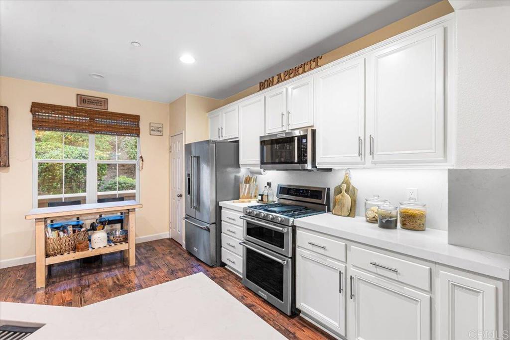 1101 Goddard Street San Marcos, CA 92078 - Photo 22 of 38 a kitchen with stainless steel appliances a stove top oven a sink a refrigerator and white cabinets with wooden floor