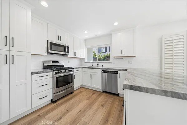 a kitchen with stainless steel appliances white cabinets a sink a stove a microwave and wooden floors