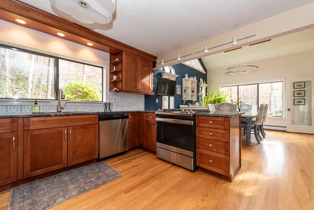 a kitchen with stainless steel appliances granite countertop a refrigerator a stove a sink a dining table and chairs with wooden floor