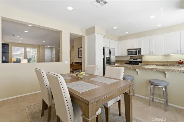 a kitchen with stainless steel appliances granite countertop a dining table chairs refrigerator and microwave