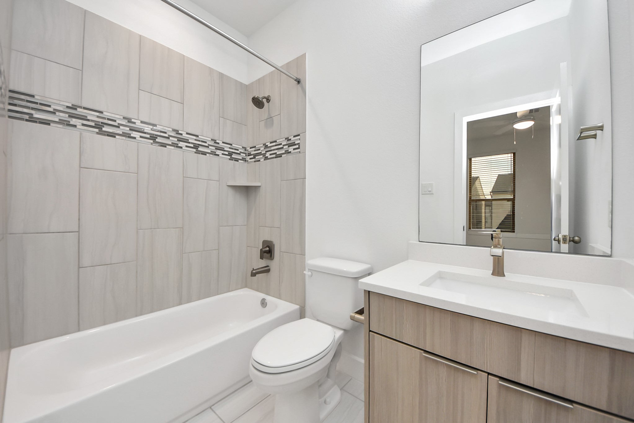 18716 Centro Main Street Conroe, TX 77385 - Photo 44 of 50 Full bathroom featuring a tiled tub/shower surround with decorative accent band, modern fixtures, and a sleek vanity with quartz countertop.
