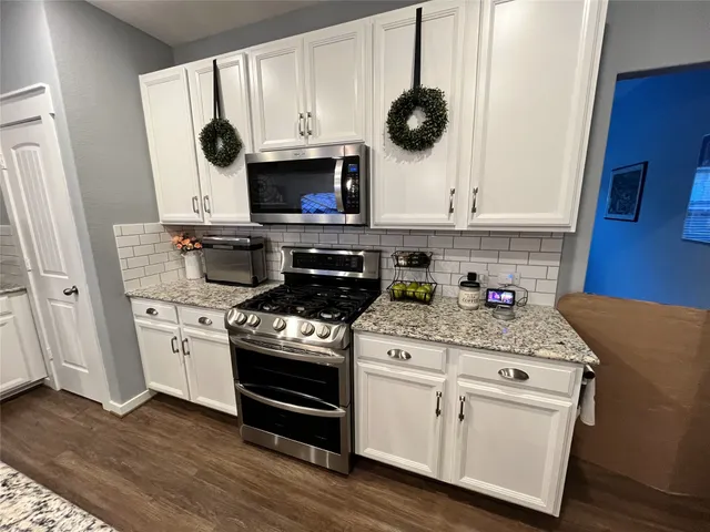 a kitchen with stainless steel appliances granite countertop a dining table chairs refrigerator and microwave