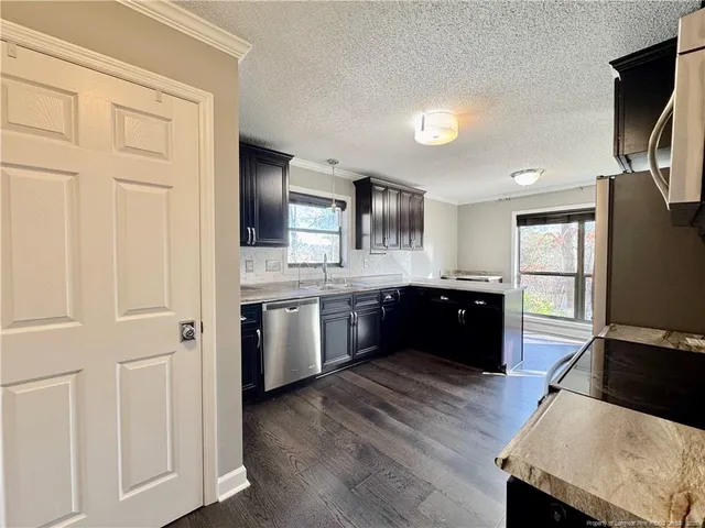 a large kitchen with granite countertop a refrigerator a sink dishwasher and white cabinets with wooden floor