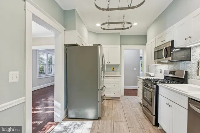 a kitchen with stainless steel appliances granite countertop a refrigerator a stove a oven and white cabinets with wooden floors