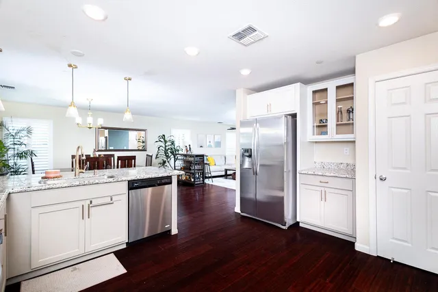 a kitchen with stainless steel appliances kitchen island granite countertop a refrigerator a sink dishwasher a stove and white cabinets with wooden floor