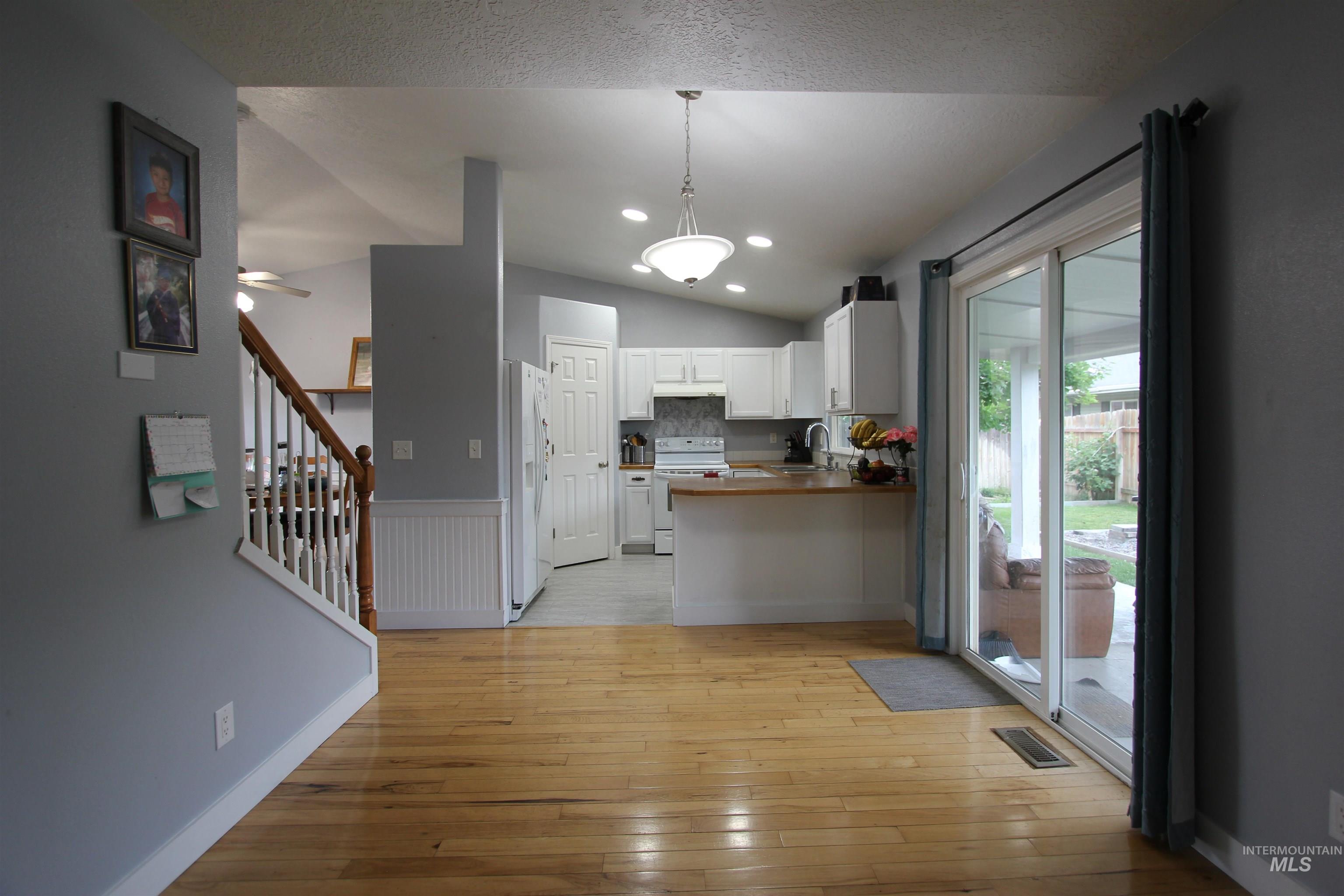 4816 Kadie Street Caldwell, ID 83607 - Photo 11 of 23 Hardwood flooring extending from the living area into the kitchen featuring white cabinetry, a wood-finish countertop, and a tile backsplash