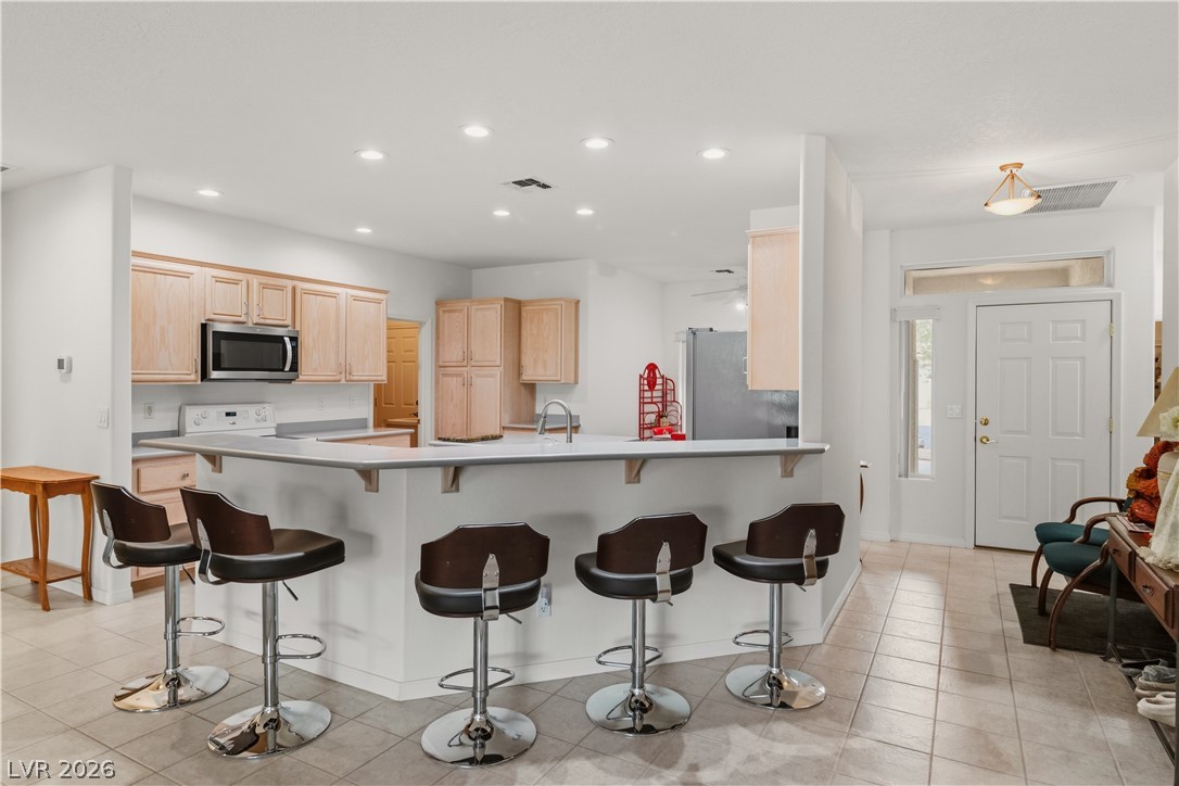 3589 Cottage Canyon Street Laughlin, NV 89029 - Photo 6 of 99 Kitchen with light wood finish cabinets, a kitchen bar, light countertops, stainless steel appliances, and a peninsula