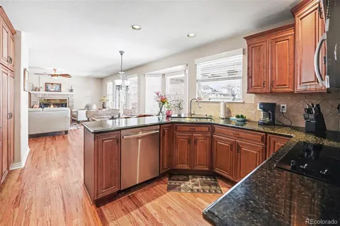 a kitchen with stainless steel appliances granite countertop wooden cabinets a sink dishwasher a stove and a refrigerator with wooden floor