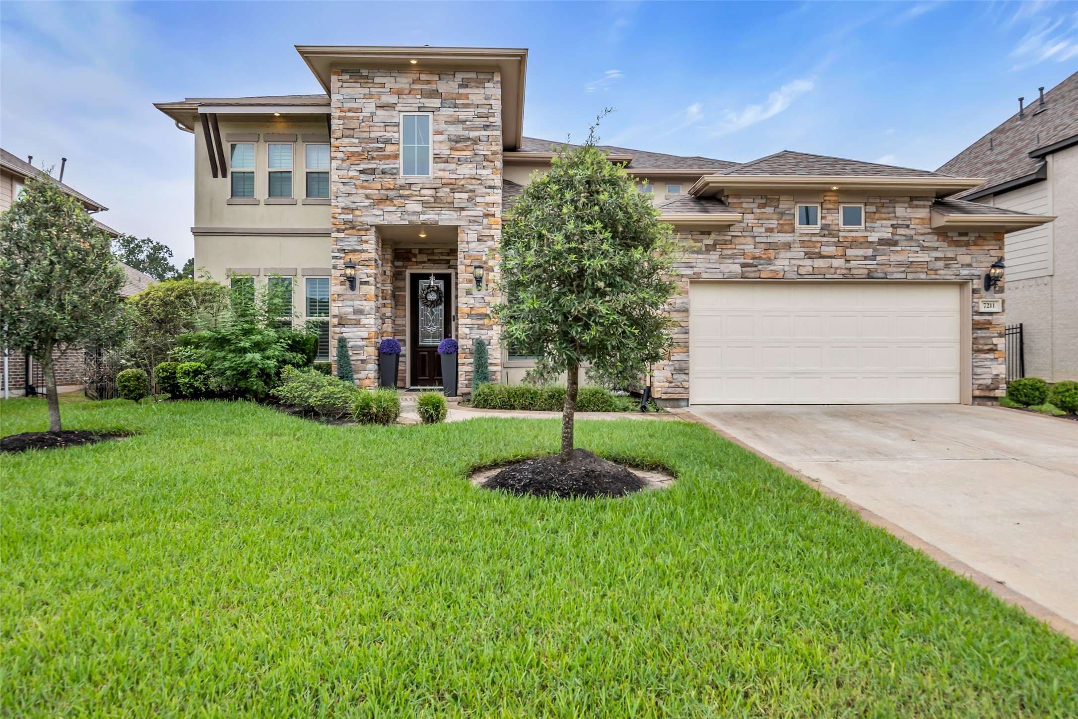 7211 Julie Pond Lane Spring, TX 77389 - Photo 4 of 45 Stunning two-story home with a charming stone facade, beautifully landscaped front yard, and a spacious driveway leading to a two-car garage, all set against a vibrant sunset backdrop.