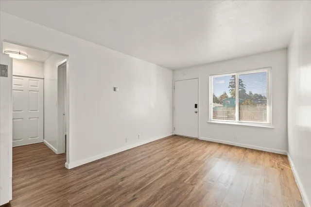 a view of an empty room with wooden floor and a window
