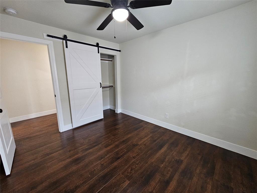 211 North Hampton Road Dallas, TX 75208 - Photo 15 of 22 Room featuring rich wood-finish flooring, a white barn door, a built-in closet with shelving, a ceiling fan with integrated lighting, and neutral wall tones
