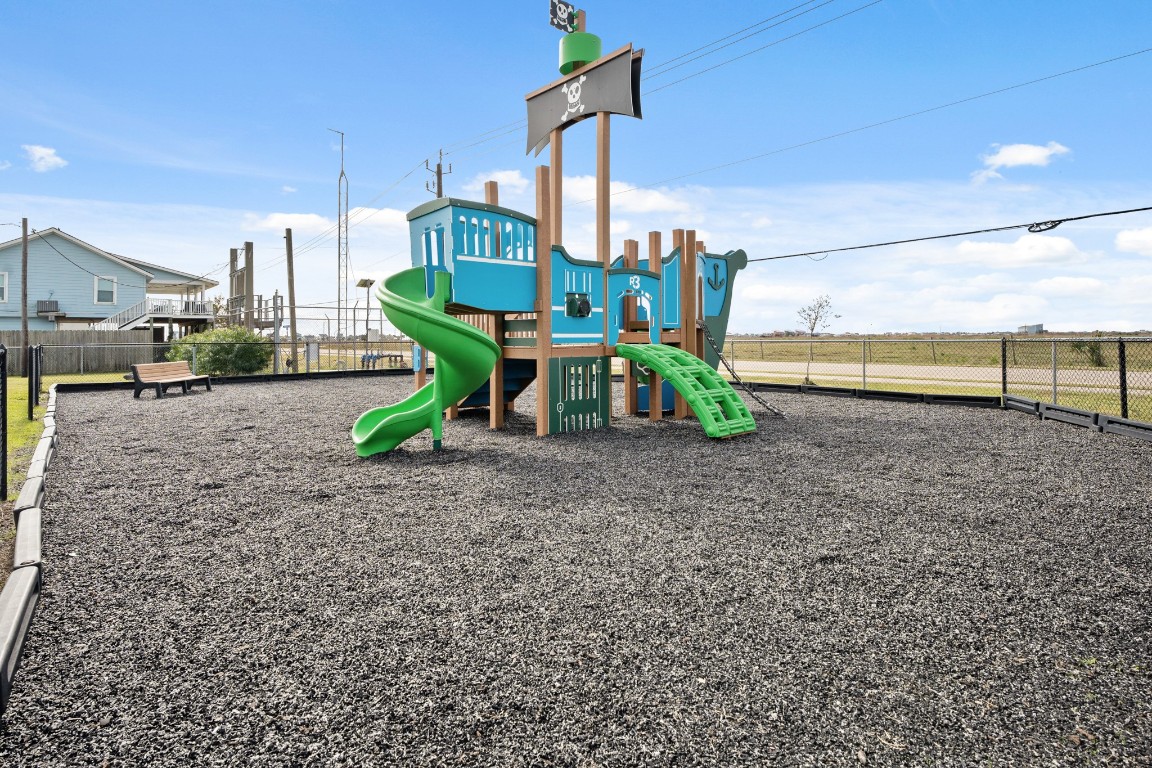 16507 Captain Kidd Road Jamaica Beach, TX 77554 - Photo 20 of 37 This photo features a fenced playground with a pirate ship-themed play structure, including slides and climbing elements, set on a gravel surface. It's perfect for families looking for a safe and fun outdoor space for children.