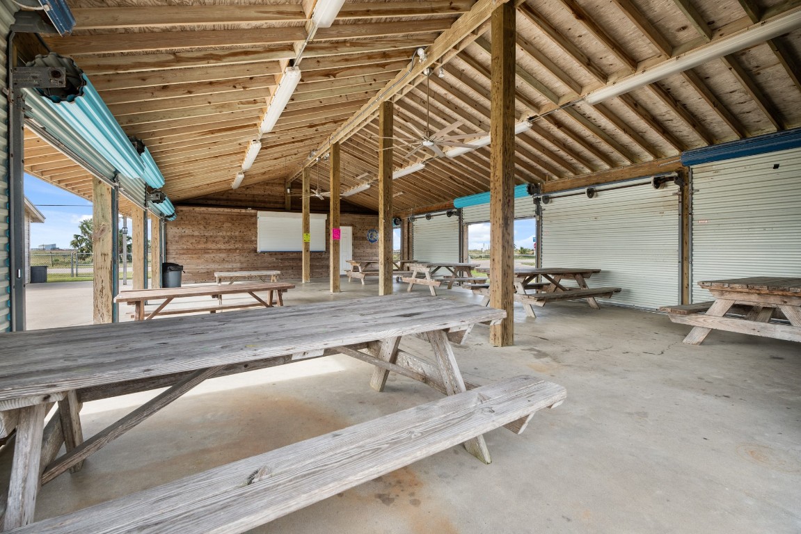 16507 Captain Kidd Road Jamaica Beach, TX 77554 - Photo 30 of 37 Neighborhood open-air pavilion with a wooden ceiling and multiple picnic tables, perfect for gatherings. It features large, roll-up doors for natural light and offers a rustic, communal atmosphere.