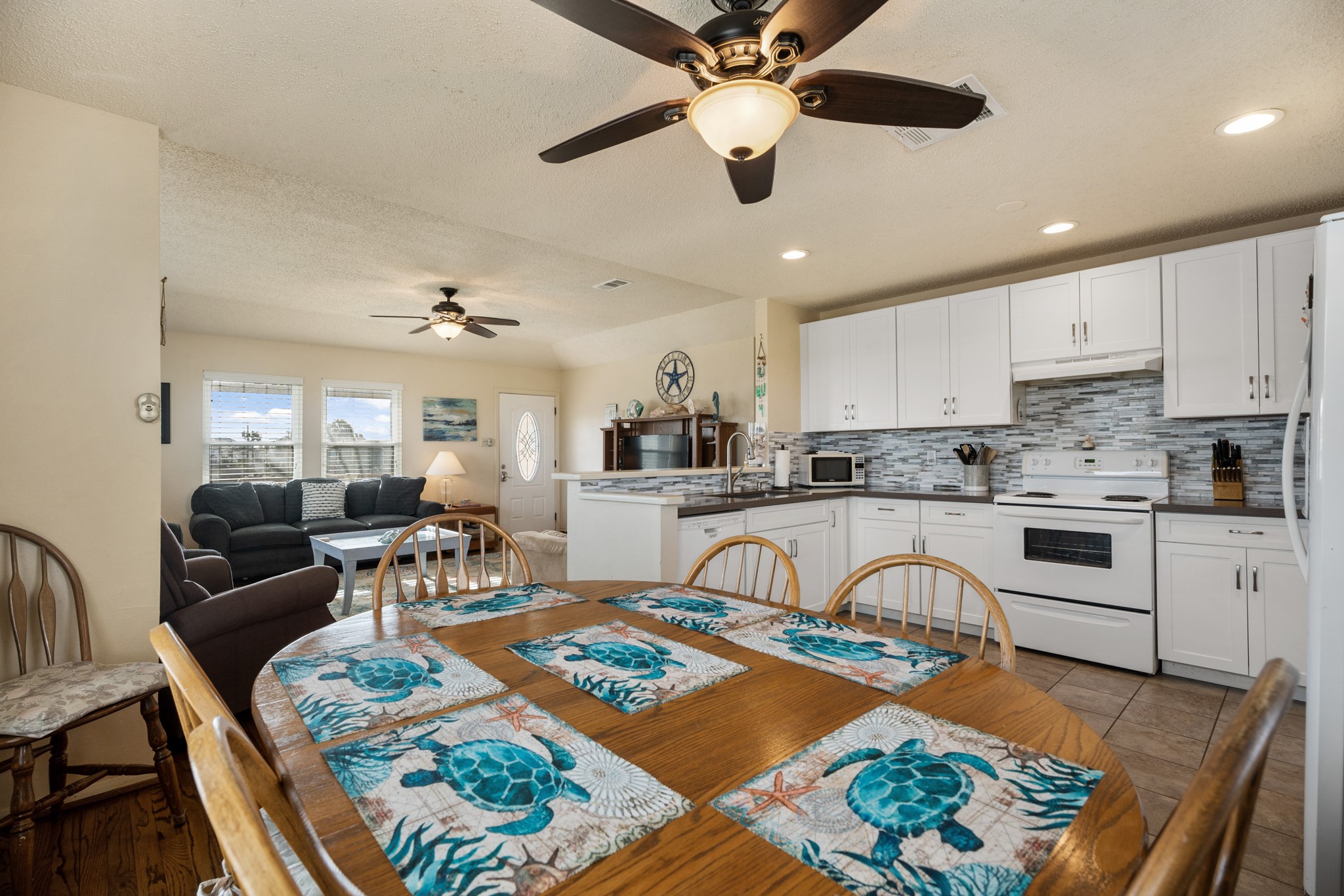 16507 Captain Kidd Road Jamaica Beach, TX 77554 - Photo 35 of 37 This open-concept space features an open floor plan to living area with a ceiling fan and natural light from large windows. The kitchen has white cabinetry, a tiled backsplash, and all appliances. A wooden dining table with room for family meals or game night.