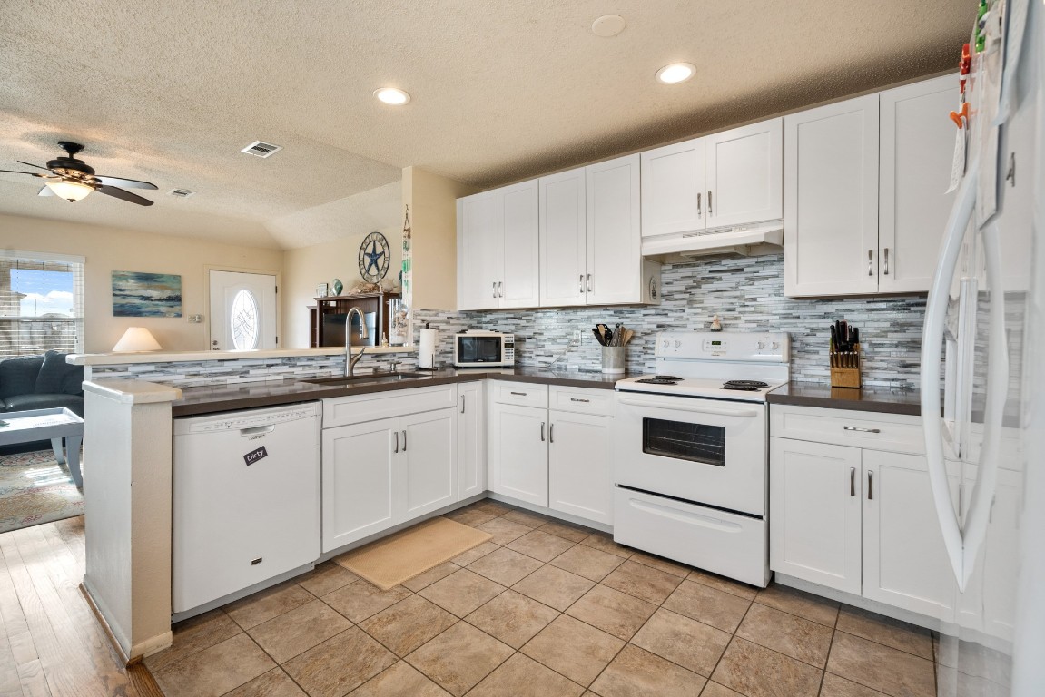 16507 Captain Kidd Road Jamaica Beach, TX 77554 - Photo 6 of 37 This bright kitchen features white cabinetry and a stylish tile backsplash. Refrigirator replaced in 2023.