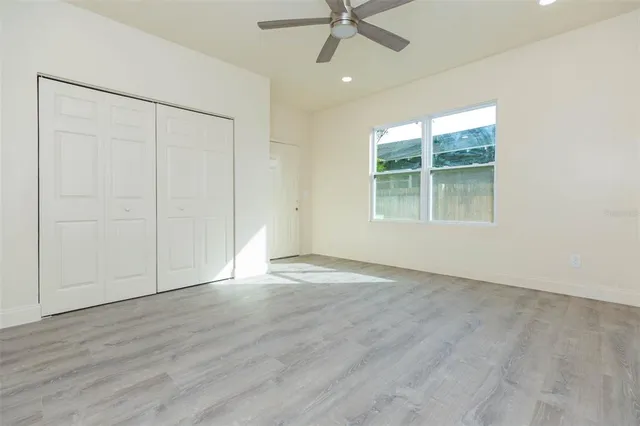 an empty room with wooden floor fan and windows