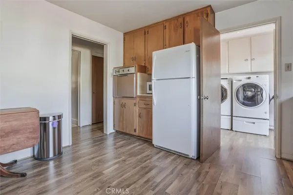 a view of a refrigerator in kitchen and an empty room with wooden floor windows