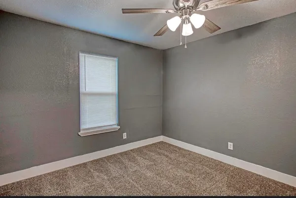 an empty room with a chandelier fan and windows