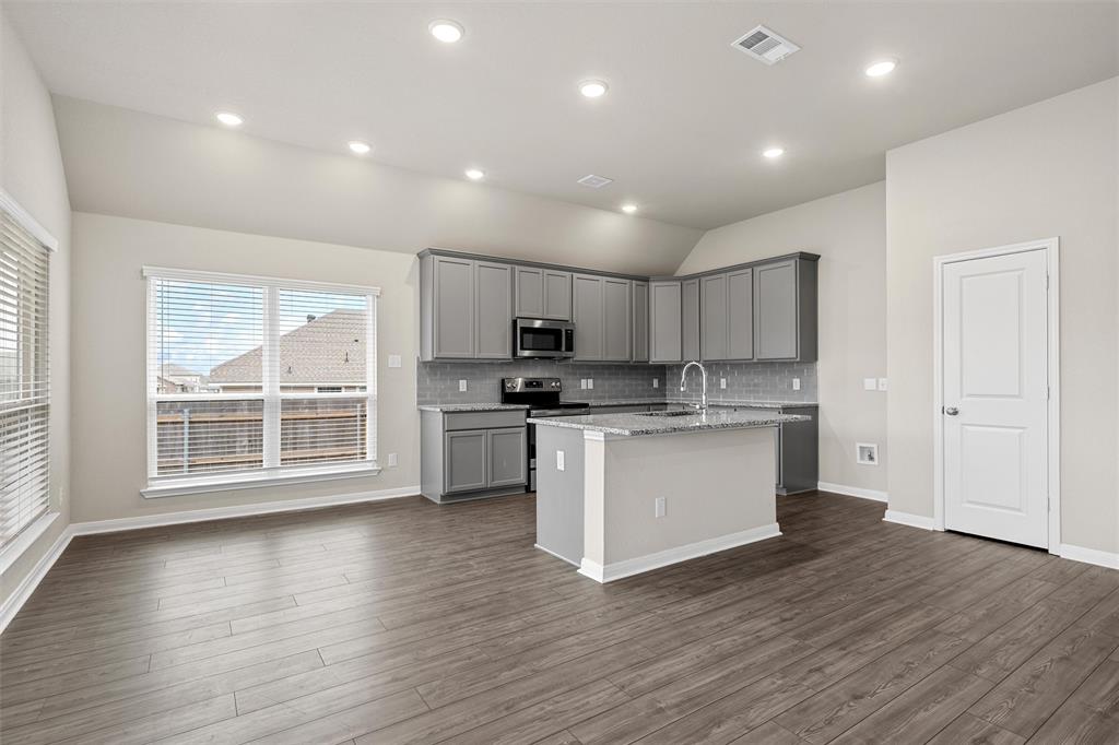 3208 Dottavio Road Lorena, TX 76655 - Photo 13 of 31 Open-concept kitchen and living area featuring grey cabinetry, stainless steel appliances, a center island with a sink, wood-finish flooring, and recessed lighting