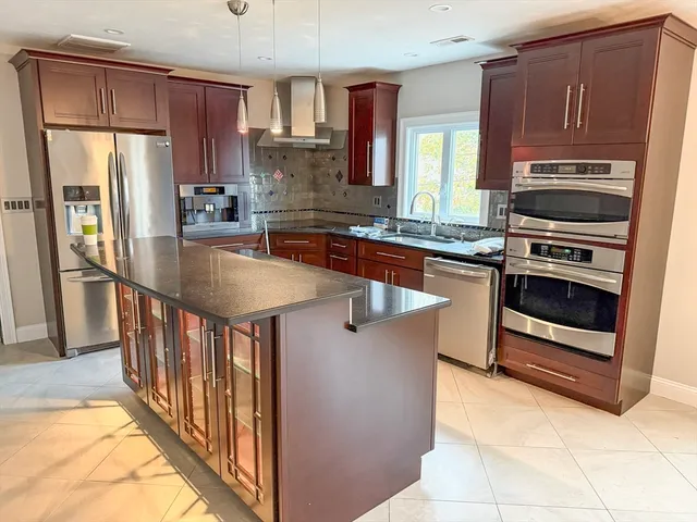 a kitchen with stainless steel appliances granite countertop a stove a refrigerator and a sink with wooden cabinets