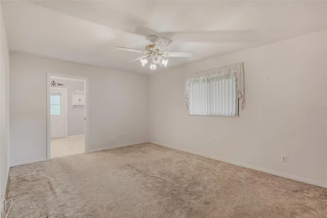 a view of an empty room with window and chandelier fan