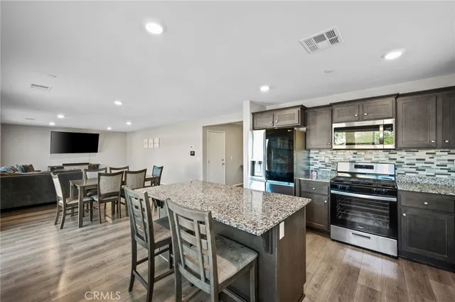 a kitchen with stainless steel appliances kitchen island granite countertop a kitchen island a stove a dining table and chairs with wooden floor