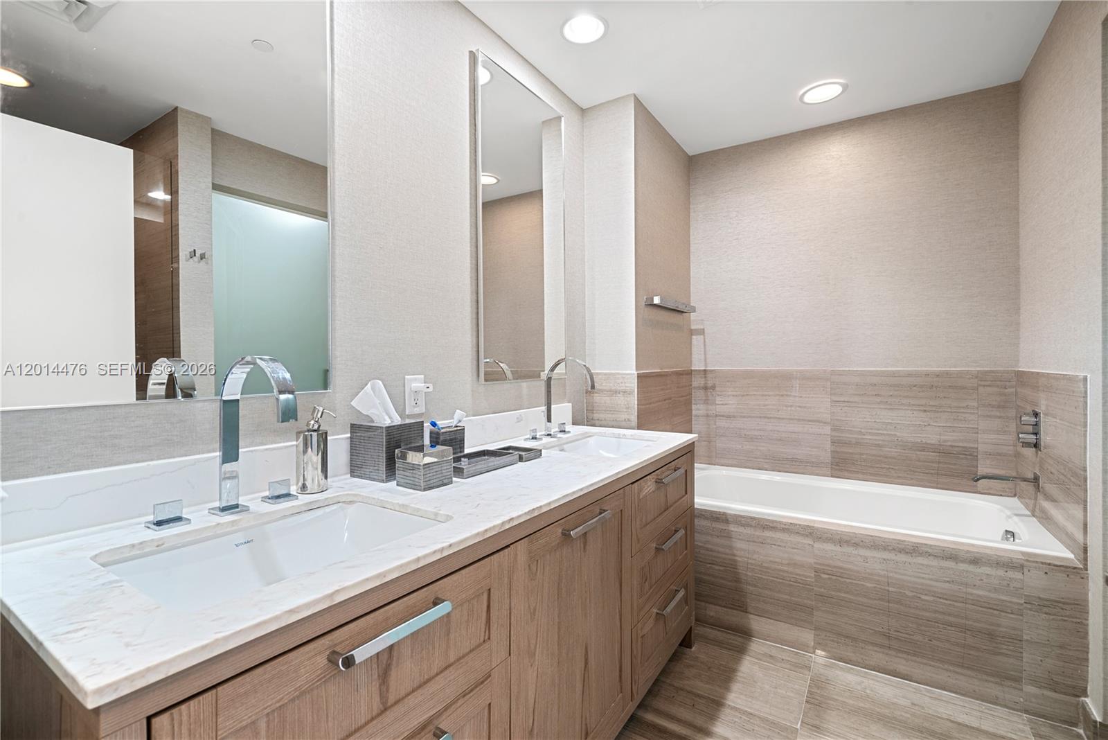 360 Ocean Drive, Unit 1106S Key Biscayne, FL 33149 - Photo 26 of 67 Primary Bathroom – The primary bath features a long wood vanity with a marble-look countertop, dual sinks, and a deep soaking tub framed by warm neutral tile. Large mirrors and recessed lighting create a bright, spa-inspired atmosphere.