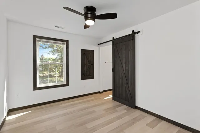an empty room with wooden floor chandelier fan and windows