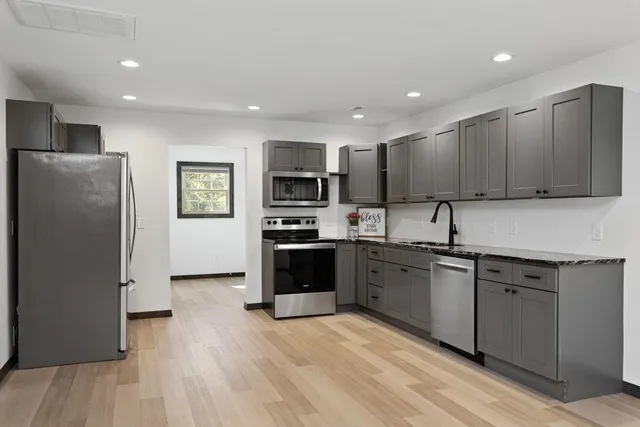 a kitchen with stainless steel appliances granite countertop a refrigerator a sink dishwasher a stove top oven a refrigerator with grey cabinets and wooden floor