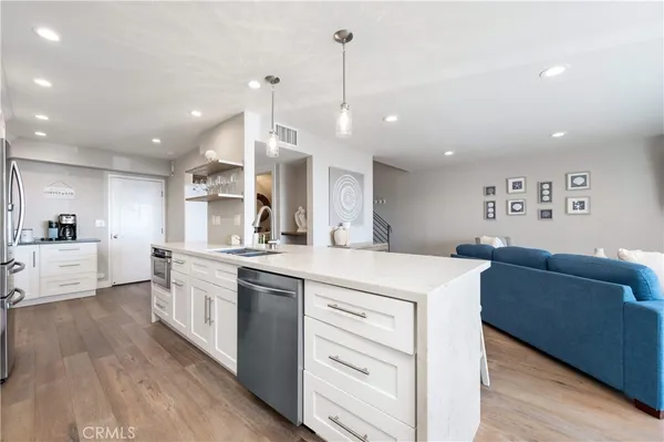 a large kitchen with stainless steel appliances a refrigerator a sink a stove and white cabinets with wooden floor