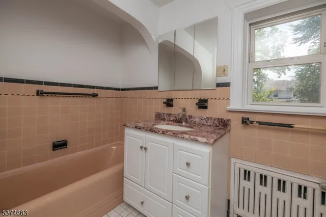 a bathroom with a granite countertop sink a mirror a bathtub and next to a window