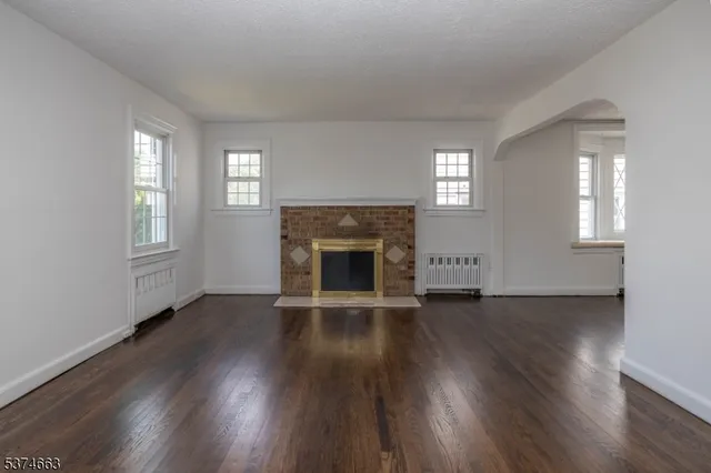 an empty room with wooden floor fireplace and windows