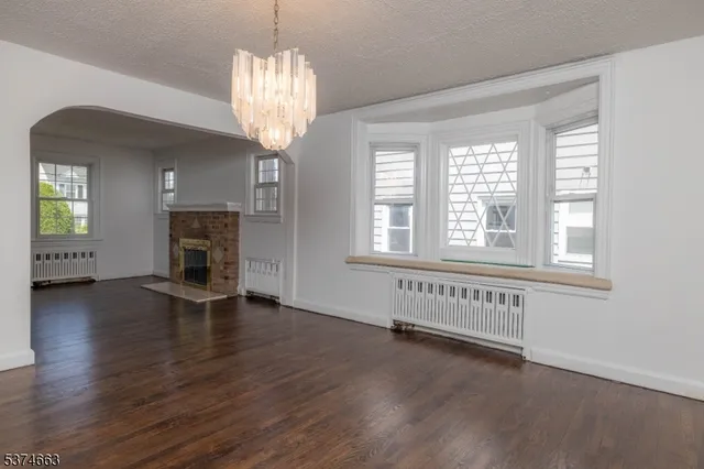 an empty room with wooden floor chandelier and windows