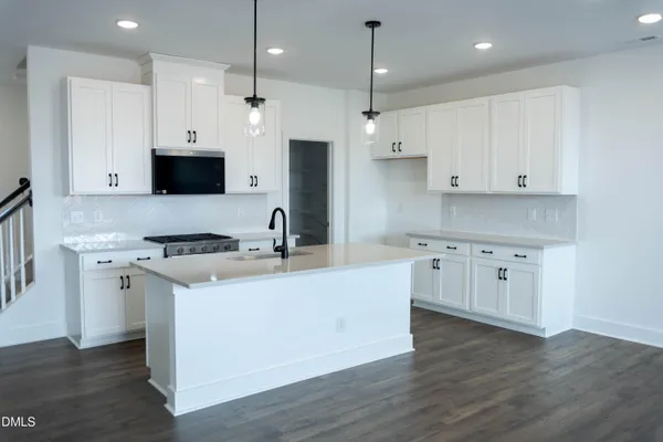 a large kitchen with stainless steel appliances granite countertop a stove a sink a refrigerator and white cabinets with wooden floor