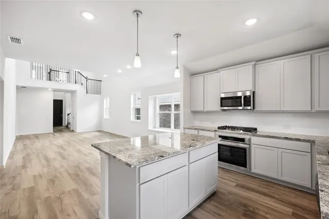 a kitchen with stainless steel appliances granite countertop a stove top oven a sink dishwasher and a refrigerator with wooden floor