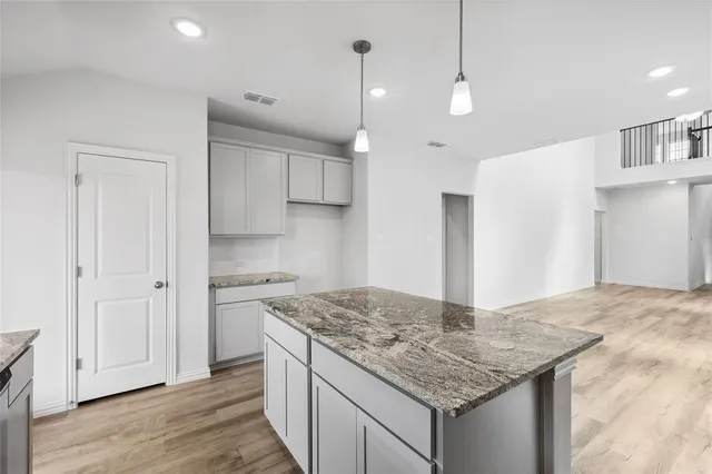 a kitchen with kitchen island granite countertop a wooden floor and a refrigerator