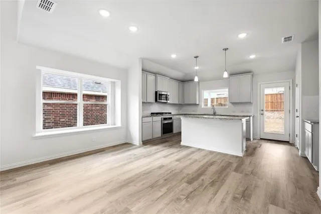 a large kitchen with stainless steel appliances granite countertop a stove a sink dishwasher a refrigerator white cabinets and wooden floor next to a window