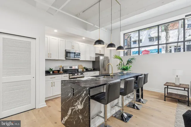 a kitchen with stainless steel appliances kitchen island granite countertop a stove a refrigerator a dining table and chairs with wooden floor