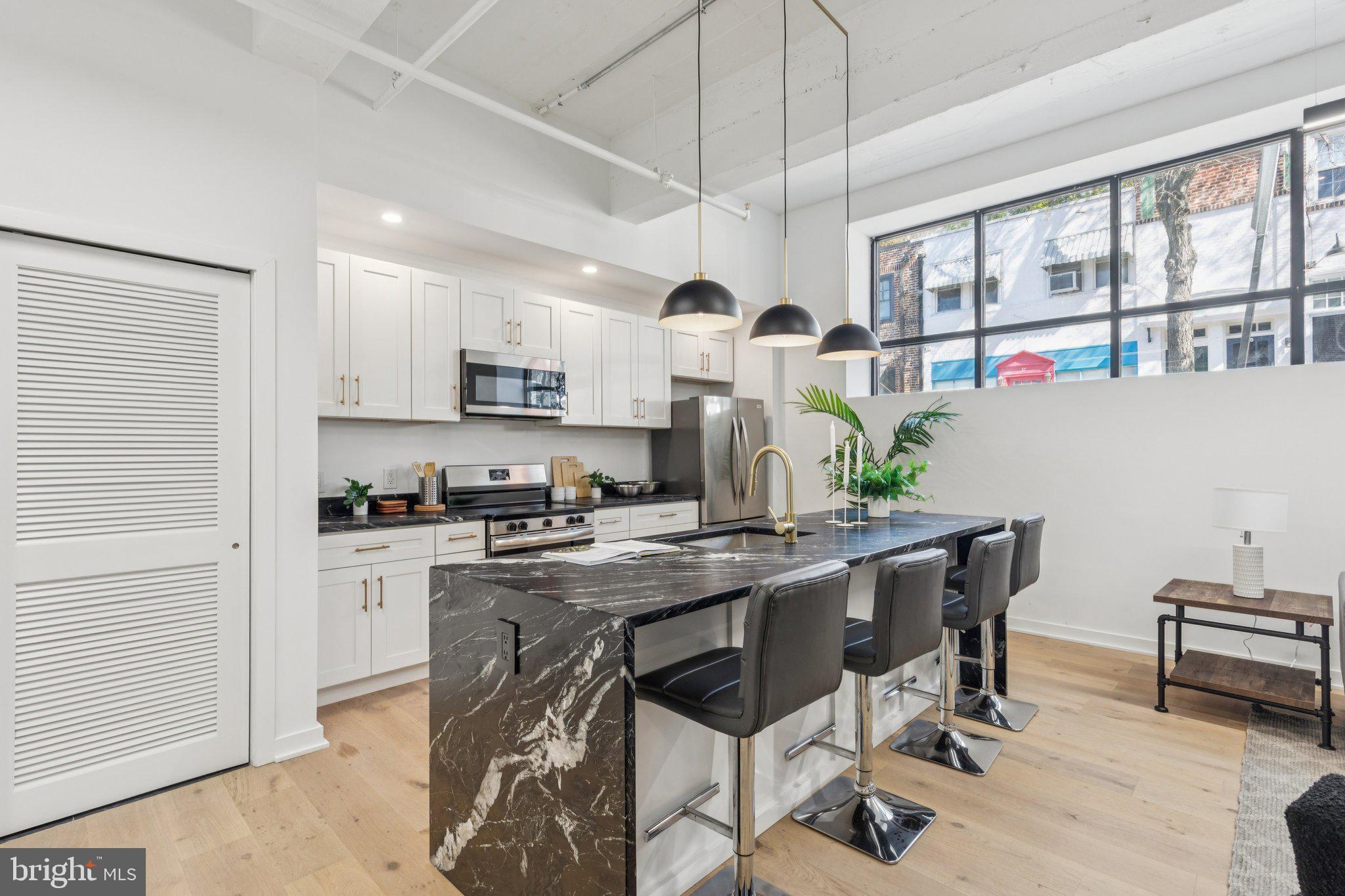 36 North Narberth Avenue, Unit 1C Narberth, PA 19072 - Photo 26 of 36 a kitchen with stainless steel appliances kitchen island granite countertop a stove a refrigerator a dining table and chairs with wooden floor
