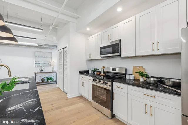 a kitchen with stainless steel appliances granite countertop a stove a sink dishwasher and a microwave oven with white cabinets