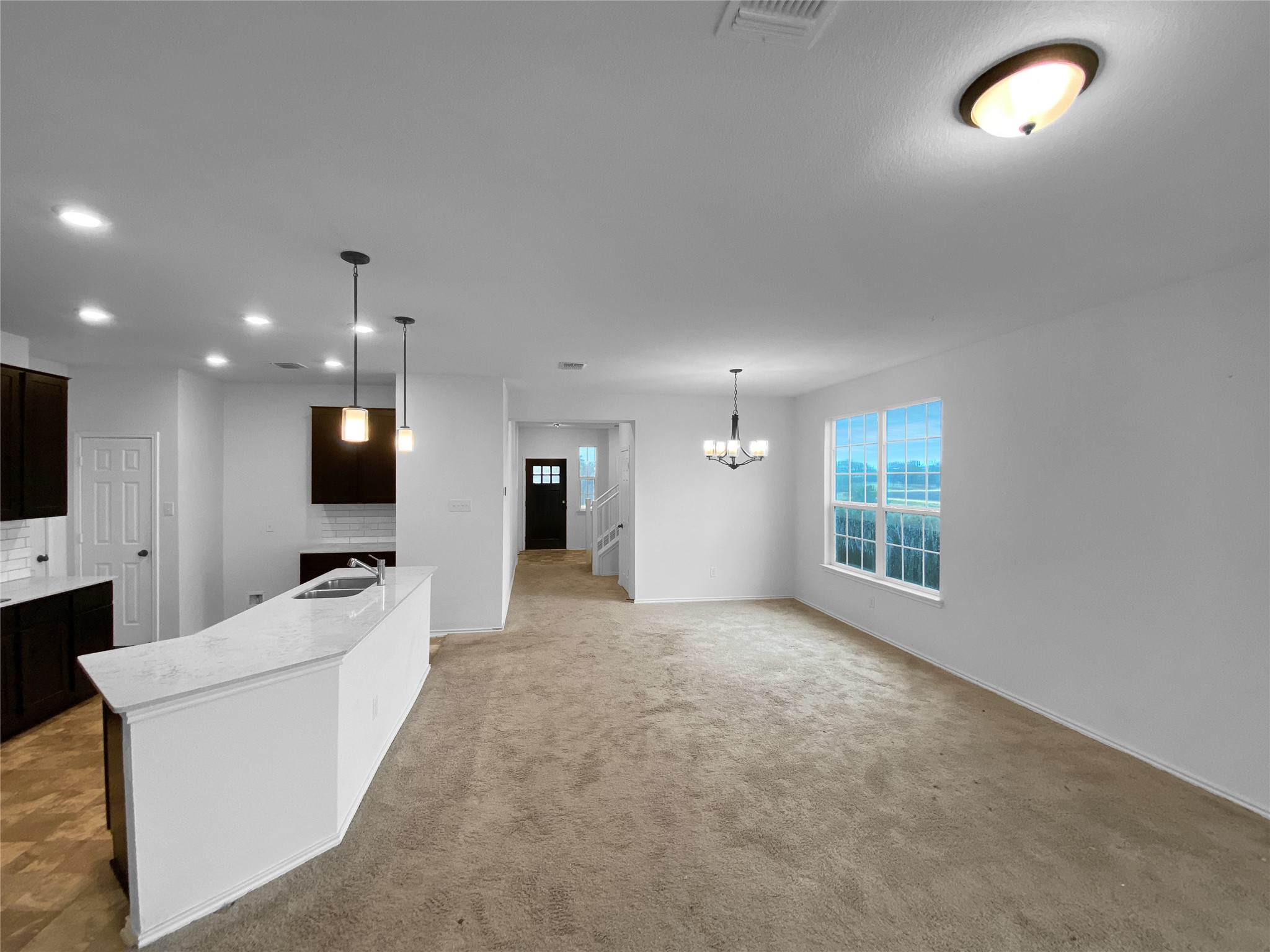 932 Yellow Ribbon Trail Jarrell, TX 76537 - Photo 6 of 26 Kitchen with dark wood finish cabinetry, an island with sink, light stone countertops, suspended lighting, and light colored carpet
