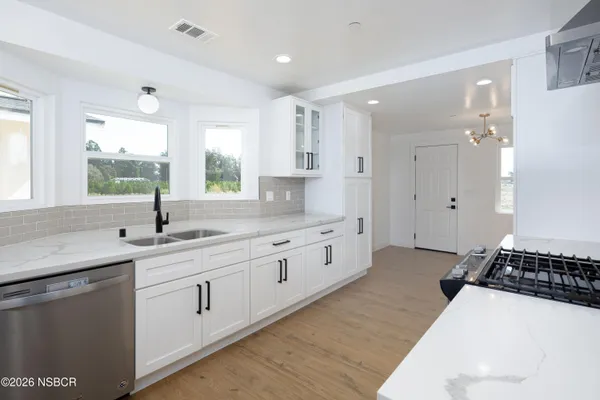 a large white kitchen with a lot of white cabinets and wooden floor