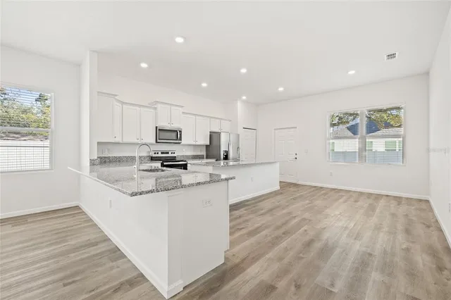 a large kitchen with granite countertop white cabinets and stainless steel appliances